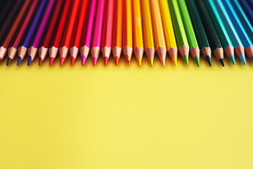 Line of colored pencils on yellow background top view. Rainbow palette wood pencils.