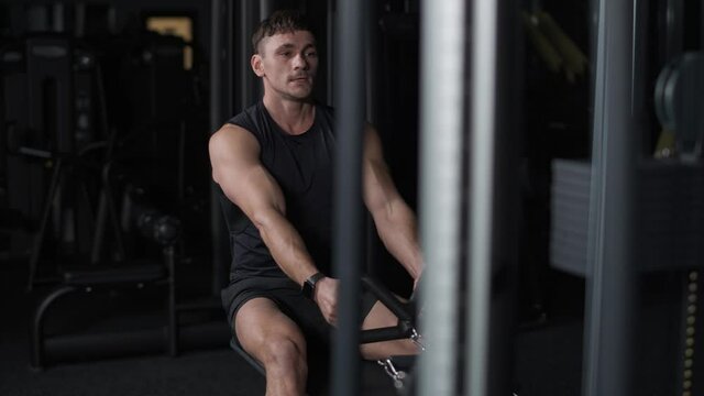 Athletic man in the gym lifting blocks on rowing machine, training on block device, cinematic lighting, 4k slow motion.