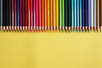 Line of colored pencils on yellow background top view. Rainbow palette wood pencils.