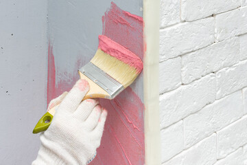 The builder applies an adhesive primer with a fine-grained quartz filler to the wall with a brush...