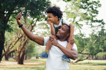 happy black people father and son riding on the father back selfie in the park