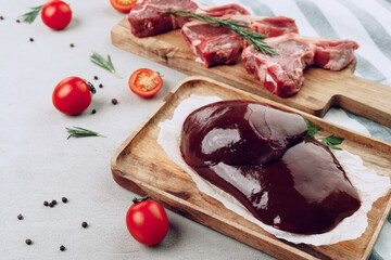 Raw beef liver and beef steaks on wooden cutting board
