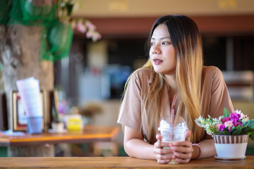 Beautyful asian women sitting in the coffee cafe and looking something. Asian girl in brown dress drinking ice coffee.