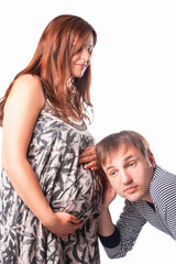 Portrait of Caucasian Man Listening His Pregnant Wife Belly with Surprised Expression. Against White