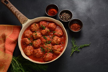 Boulettes de Poisson, Fried Fish Balls in Tomato Sauce in a white dish on a concrete table with ingredients