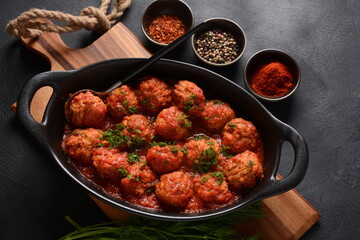 Boulettes de Poisson, Fried Fish Balls in Tomato Sauce in a black dish on a concrete table with ingredients