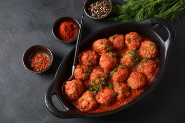 Boulettes de Poisson, Fried Fish Balls in Tomato Sauce in a black dish on a concrete table with ingredients