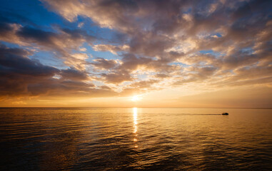 Obraz premium Calm sea with sunset sky and sun through the clouds over.