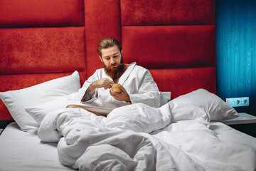 Attractive man with a long stylish mustache and beard wearing a white robe in a hotel and holding a cream. Spa concept