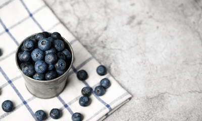 Fresh blueberries in a small metal bucket surrounded with some berries on a checked napkin. Top view. Rustic.