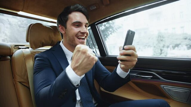 Excited business man having success at online meeting in business car.