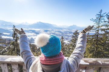 Obraz premium Happy young woman is raising her hands on the mountain, enjoying the view over Salzburg. Winter time on Gaisberg, Salzburg, Austria