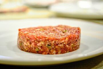 Steak tartare in the foreground on a white plate and in the background other blurred planes