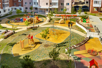 Top view of empty new modern children playground in courtyard of high-rise residential buildings in sunny summer day
