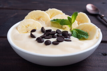 Healthy breakfast, dessert with milk yogurt banana and chocolate on a plate. Dark wooden background.