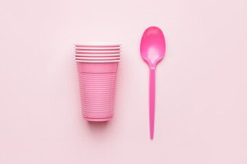 Plastic cups and spoon on color background