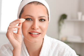 Beautiful young woman with sponge applying makeup at home