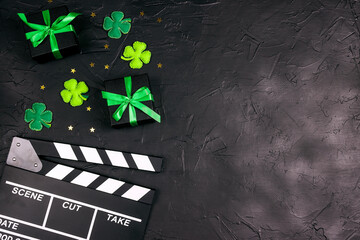 Movie clapper board with decorative clover leaves, gift boxes and gold stars on black background...