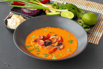 Tom Yam Thai soup in black bowl on gray table