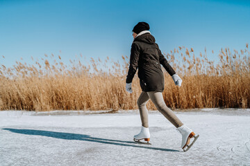 Young woman ice skating outdoors on a pond. Woman figure skating on frozen lake.