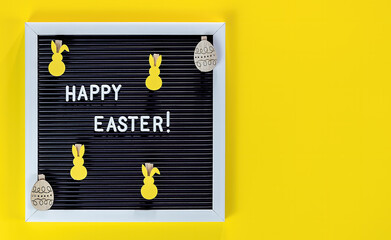 Easter bunny and letter board on yellow background. Flat lay of Easter celebration concept.