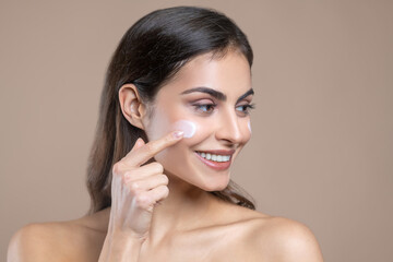 Woman applying cream on cheek with her finger