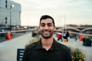 Mixed race male standing on boardwalk smiling enjoying evening walk 