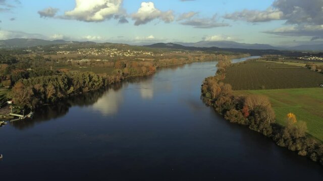 An aerial view of a tranquil river with trees on both sides near a greenfield in 4K