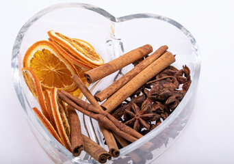 Slices of dried oranges, cinnamon and cardamom in a heart-shaped glass dish