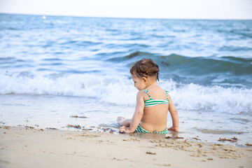 Fototapeta na wymiar little toddler girl sitting on the beach and looking at the waves. back view