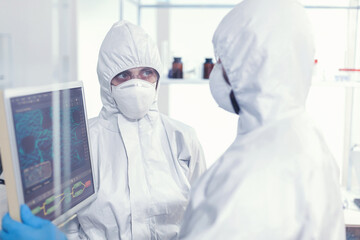 Fototapeta premium Scientists coworkers in coverall discussing about virus evolution in equipped laboratory pointing on computer desktop. Doctors examining virus evolution using high tech researching diagnosis against