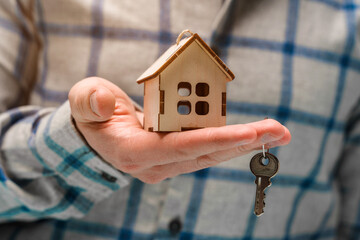 A hand holds a wooden house as a symbol of caring and buying real estate