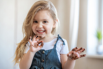 Portrait of adorable blonde little girl eating chocolate. Close up of toddler child with dirty...