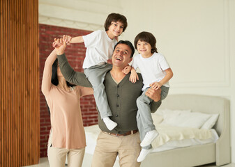 Portrait of joyful latin family, parents and little twin boys smiling at camera while posing...