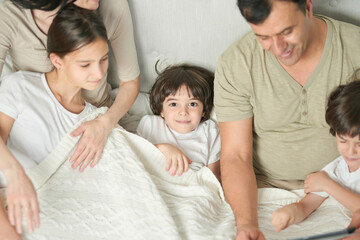 Portrait of cute little latin boy smiling at camera while spending time with his siblings and parents, staying in bed in the morning