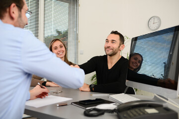 Young couple signing documents in a business bank insurance office with a professional real estate agent shaking hands