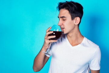 Handsome young guy is drinking wine. A man in white clothes on a deep background. Holidays and weekends.