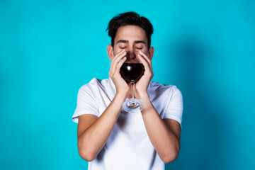 Handsome young guy is drinking wine. A man in white clothes on a deep background. Holidays and weekends.