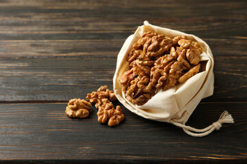 Cotton bag with tasty walnuts on wooden background