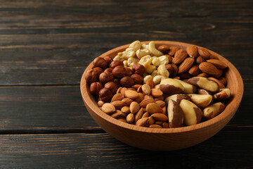Bowl with different nuts on wooden background