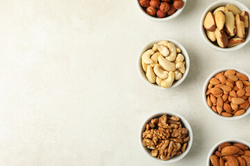 Bowls with different nuts on white textured background, space for text