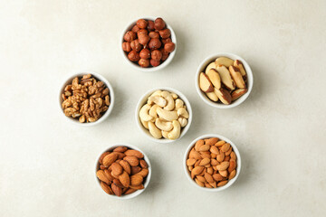 Bowls with different nuts on white textured background, top view