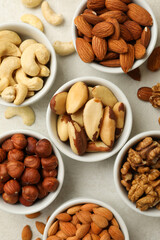 Bowls with different nuts on white textured background, top view
