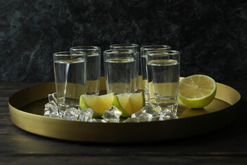 Tray with shots, lime slices and ice cubes on wooden background