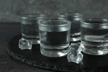 Tray with wet shots of vodka and ice on dark table