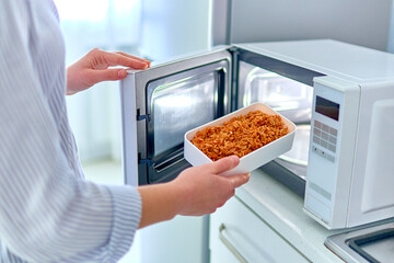 Female hands warming up a container of food in the modern microwave oven for snack lunch at home