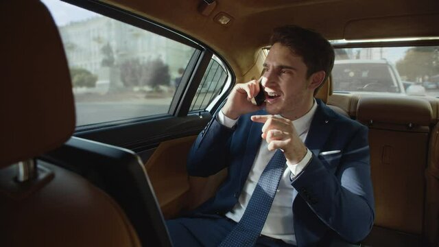 Strict business man swearing on mobile phone in back seat of luxury automobile.