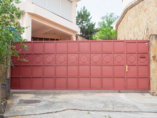 A red iron fence with a wicket gate, geometric pattern and sharp spiers encloses a modern...
