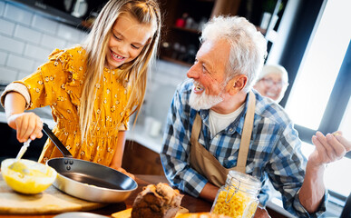Happy young girl and her grandfather cooking together in kitchen