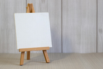 White canvas on a small easel on a light wooden background, close up, blank sheet concept with copy...
